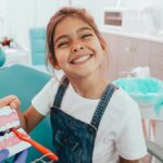 Little girl smiling and holding teeth model at dentist's office