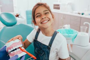 Little girl smiling and holding teeth model at dentist's office